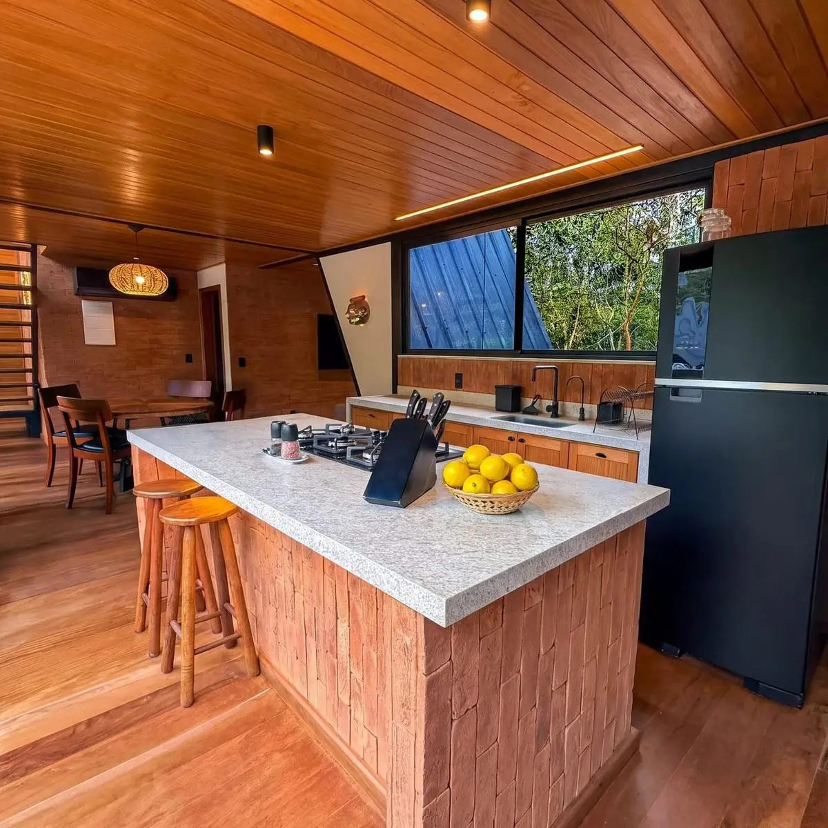 Cozinha com ilha de tijolo aparente, bancada de granito e banquetas