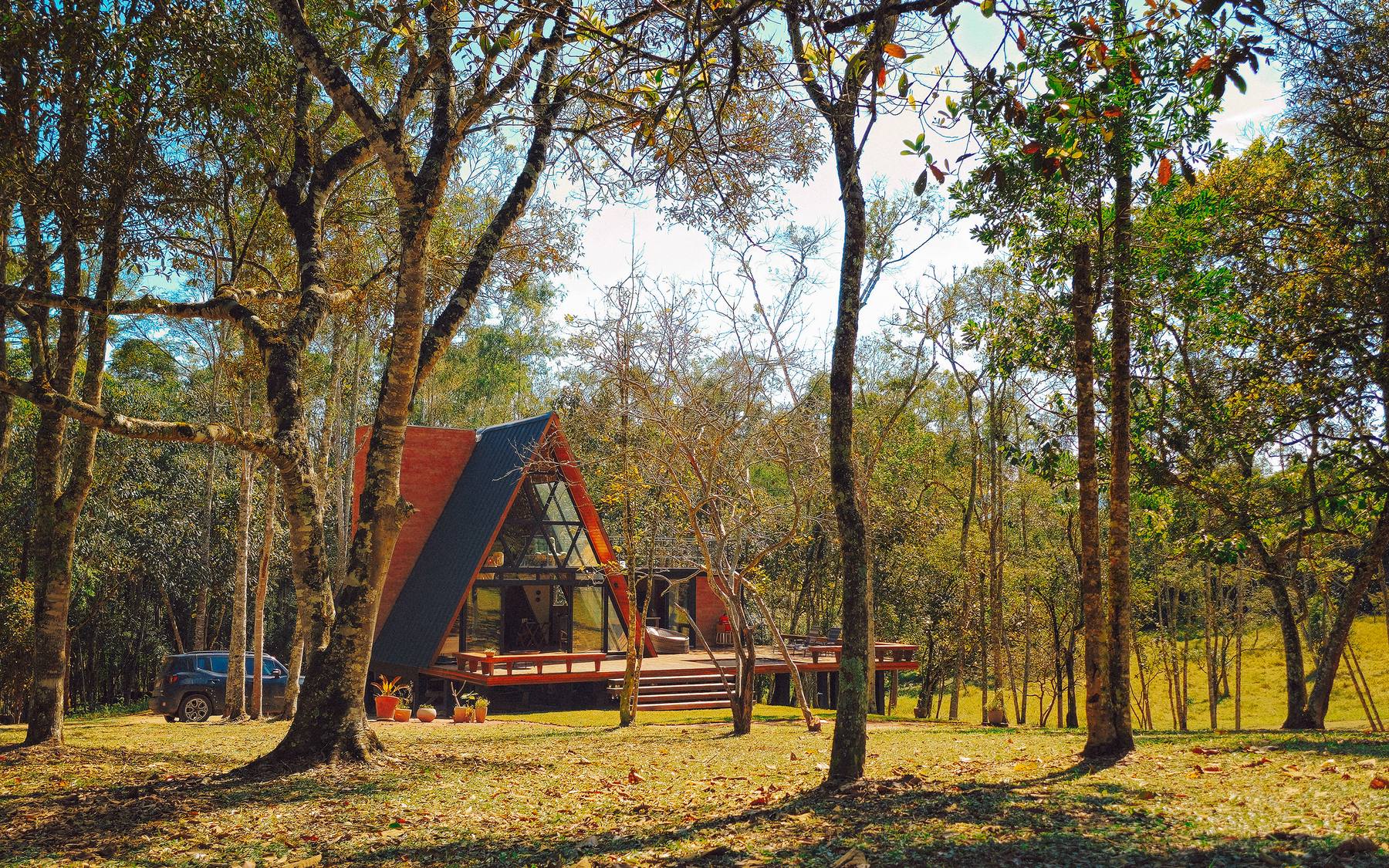 O chalé A-frame visto de longe, entre as árvores do bosque