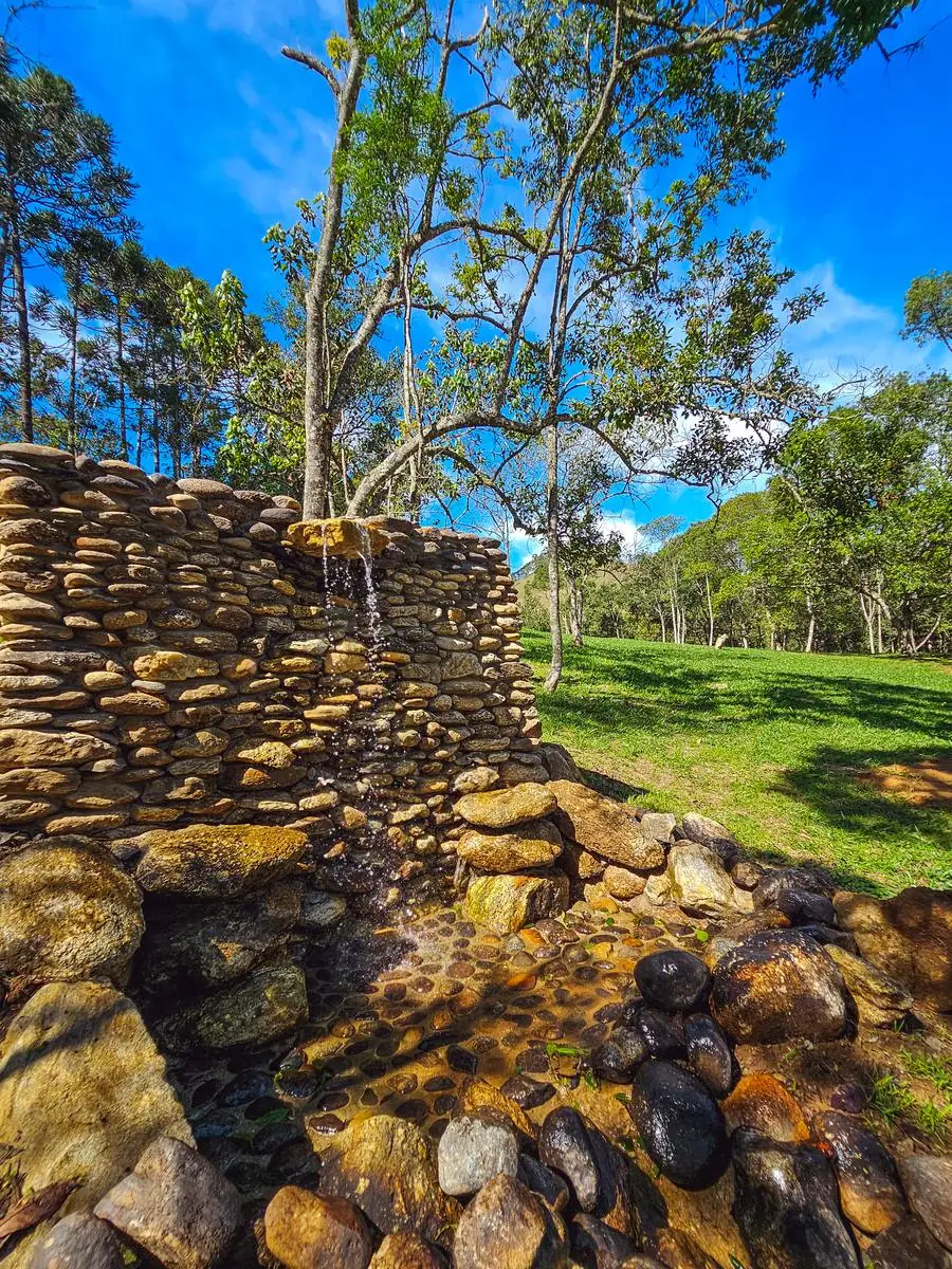 A queda d'água caindo do muro de pedras, com o gramado e as árvores ao fundo